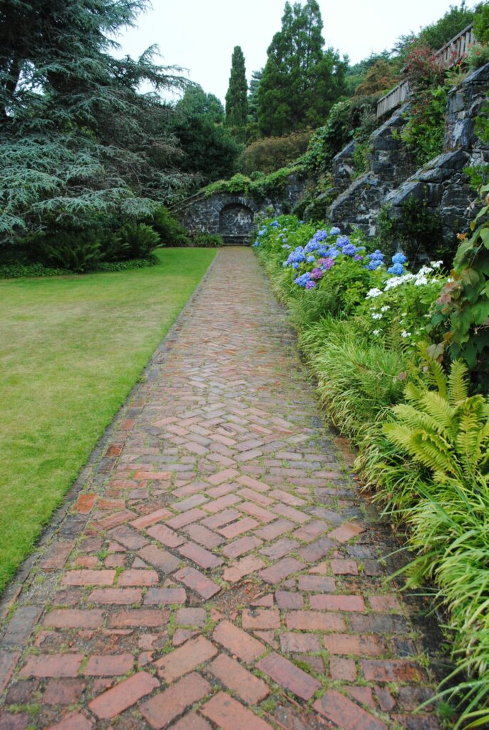 A brick path laid level with the lawn along a planted bed